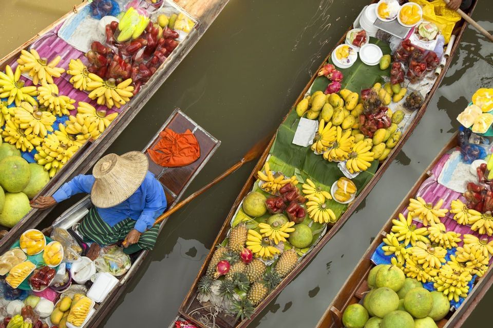 Vista aérea de un mercado flotante con varios barcos de madera llenos de frutas frescas como plátanos y piñas.