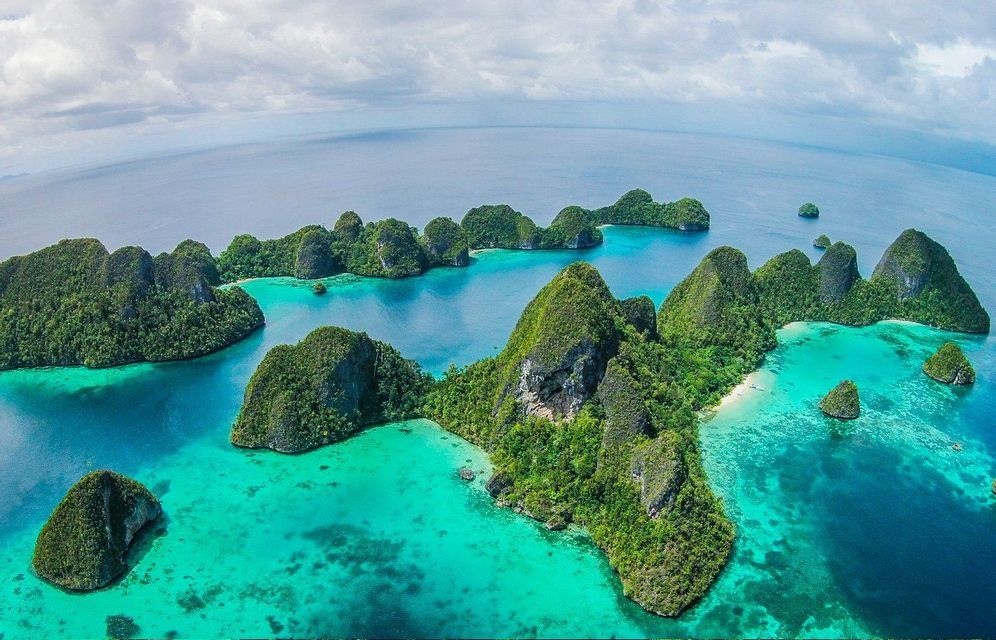 Vista aérea de un archipiélago tropical con exuberantes islas verdes sobre el océano turquesa y azul bajo un cielo nublado