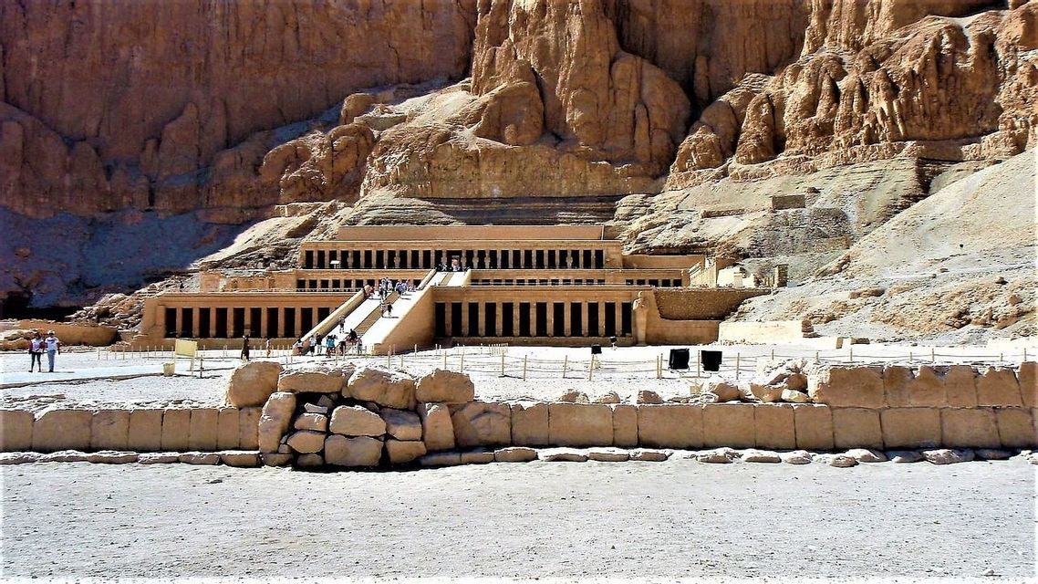 Un grande tempio a più livelli con colonnati, costruito in una scogliera rocciosa, con persone che salgono una rampa centrale in pietra.