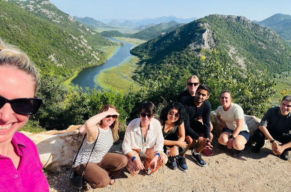 Un grupo de viaje de WeRoad posa para una foto en un mirador con vistas a un río serpenteante y un valle con colinas verdes.