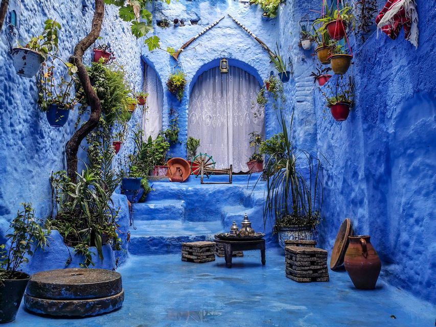 Un cortile con pareti blu testurizzate, gradini e pavimento, decorato con piante in vaso, sgabelli in pietra e un tavolino con un servizio da tè.