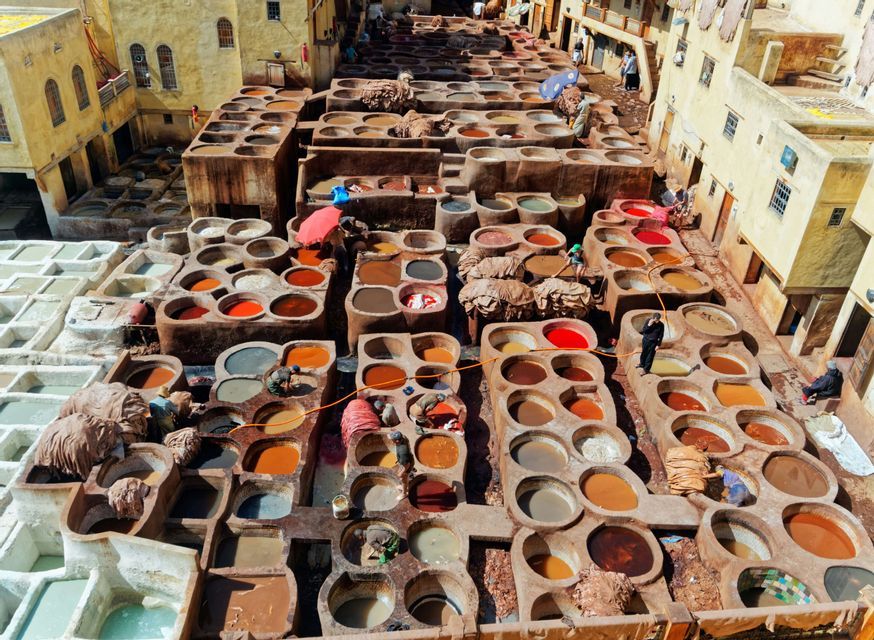 Veduta aerea di una conceria tradizionale con numerose vasche in pietra piene di tinture colorate e persone al lavoro.