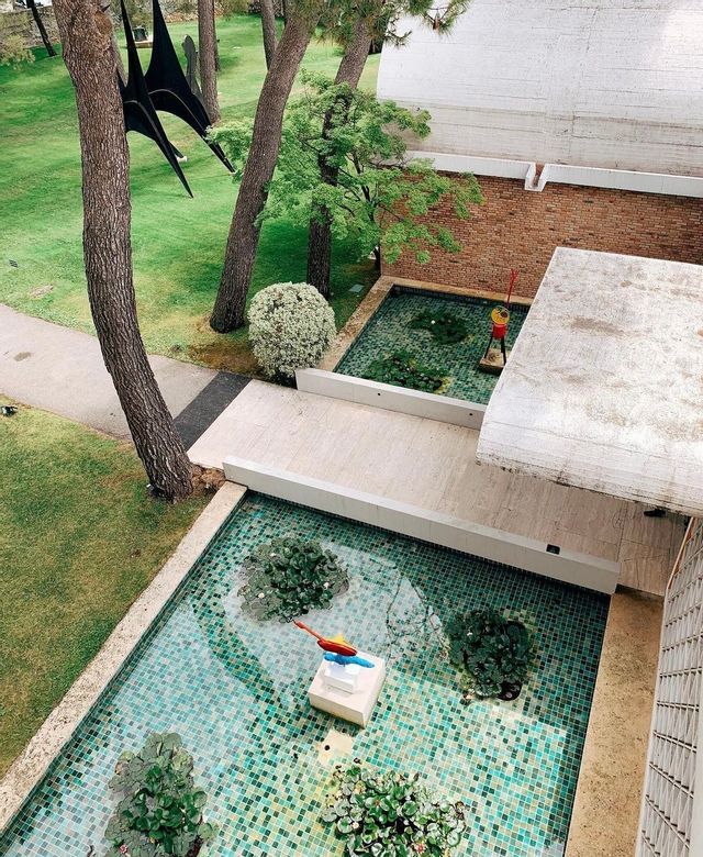 Veduta dall'alto di un moderno giardino interno, con due piscine piastrellate, sculture astratte colorate e alberi ad alto fusto.