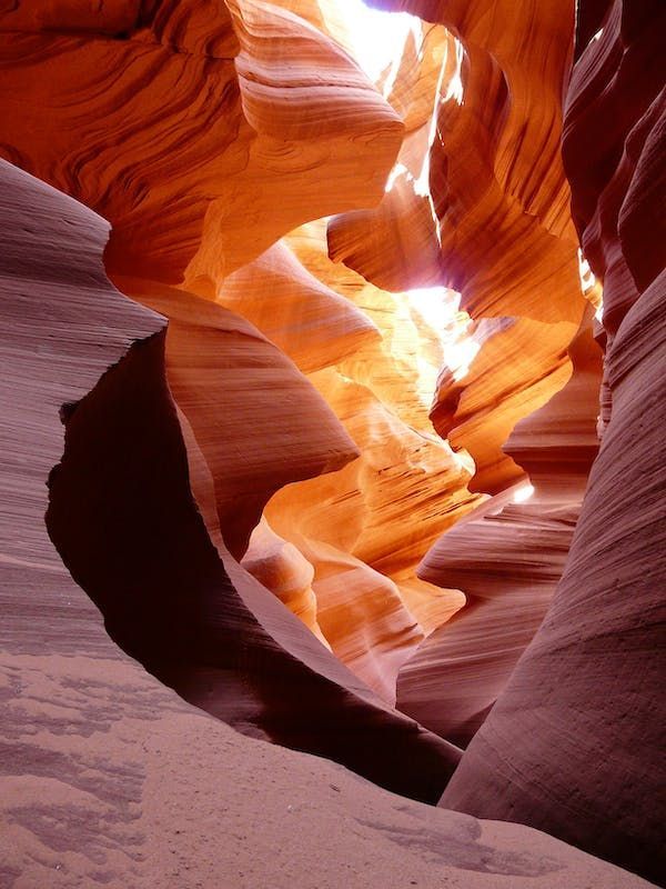 La luce del sole si riversa in uno stretto canyon a fessura, mettendo in risalto la trama ondulata delle pareti di arenaria arancione e rossa.