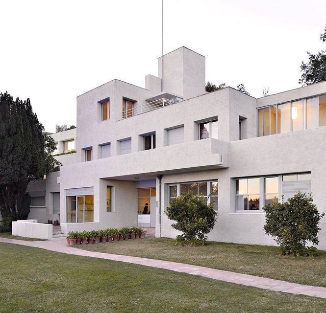 L'esterno di una casa modernista a più piani con una facciata bianca testurizzata, circondata da un prato verde e alberi.