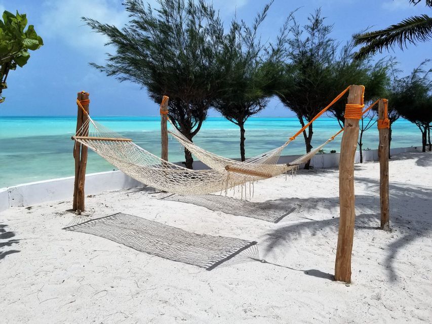Due amache vuote intrecciate pendono su una spiaggia di sabbia bianca, con l'acqua turchese dell'oceano e alberi verdi sullo sfondo.