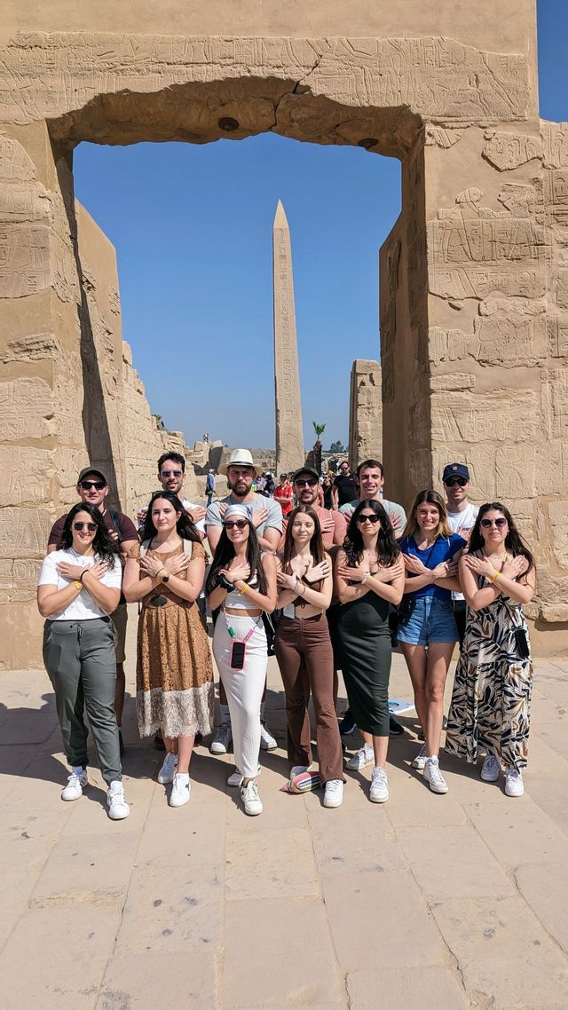 Un viaggio di gruppo WeRoad in posa con le braccia incrociate davanti a un arco in pietra con un obelisco sullo sfondo.