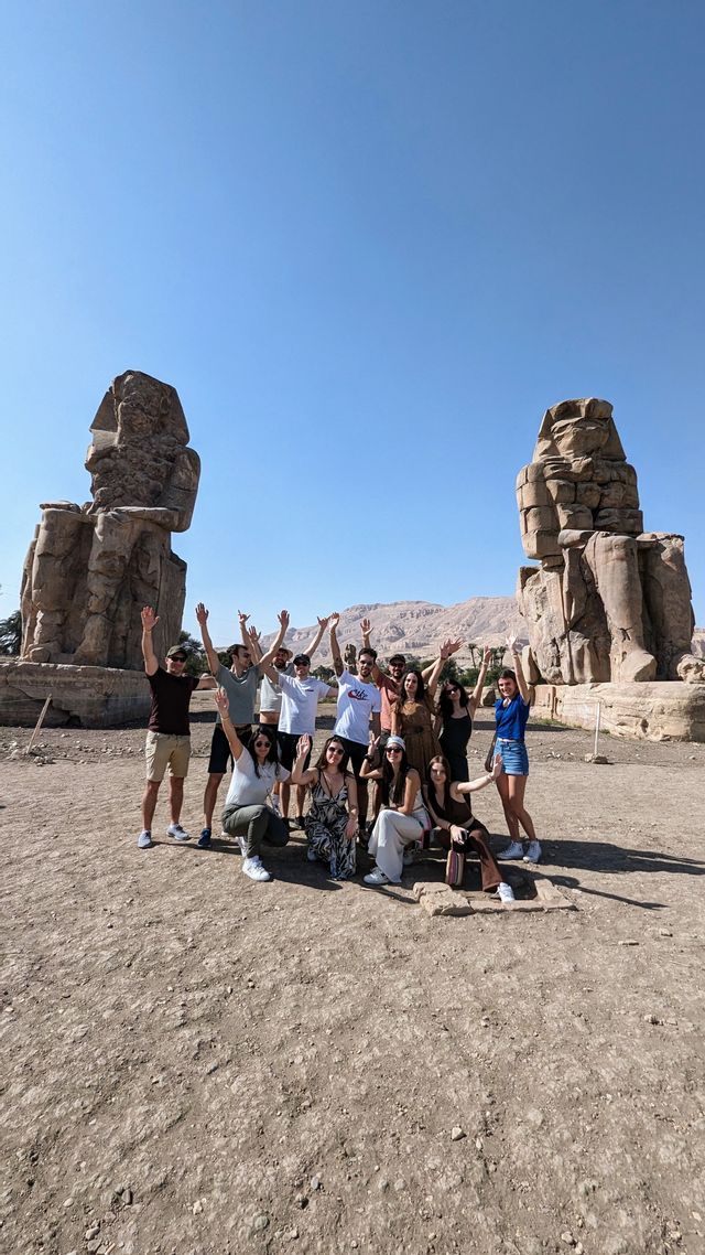 Un viaggio di gruppo WeRoad in posa per una foto davanti a due colossali statue di pietra sotto un cielo sereno.