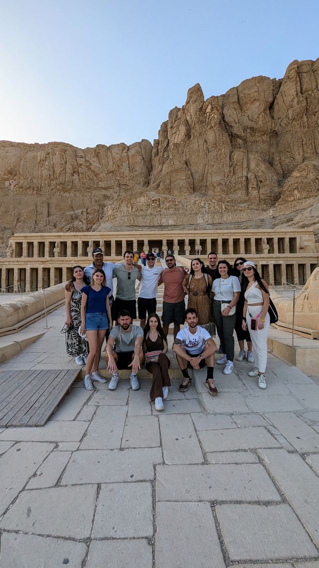 Un viaggio di gruppo WeRoad in posa per una foto su scalini di pietra davanti a un tempio scavato nella parete rocciosa.