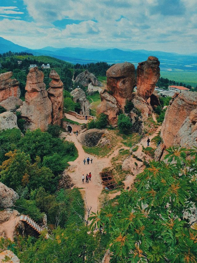 Una vista dall'alto di persone che percorrono sentieri sterrati che si snodano in una valle con grandi e particolari formazioni rocciose e alberi di un verde lussureggiante.