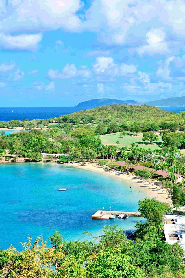 Una vista dall'alto di una baia tropicale con acqua turchese, una spiaggia sabbiosa fiancheggiata da palme e lussureggianti colline verdi.