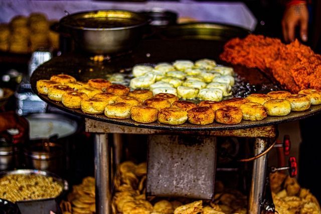 Tortitas redondas doradas y blancas se cocinan junto a comida desmenuzada naranja en una gran plancha plana en un puesto de comida callejera.