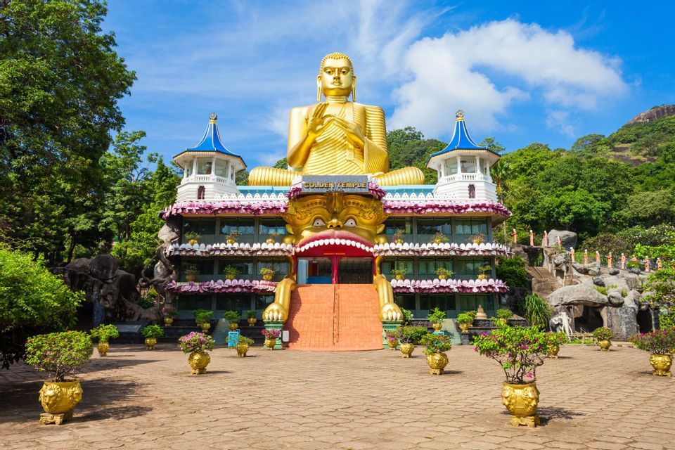 Una gigantesca statua dorata di Buddha si erge in cima all'ornato edificio del Tempio d'Oro, con scale che conducono a un grande ingresso a bocca di mostro.