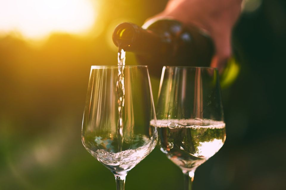 White wine is poured from a bottle into two glasses outdoors during a golden sunset.