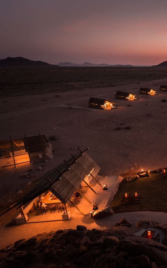 Un campo desertico illuminato con lodge rustici al tramonto, con un gruppo WeRoad che cena nell'edificio principale.