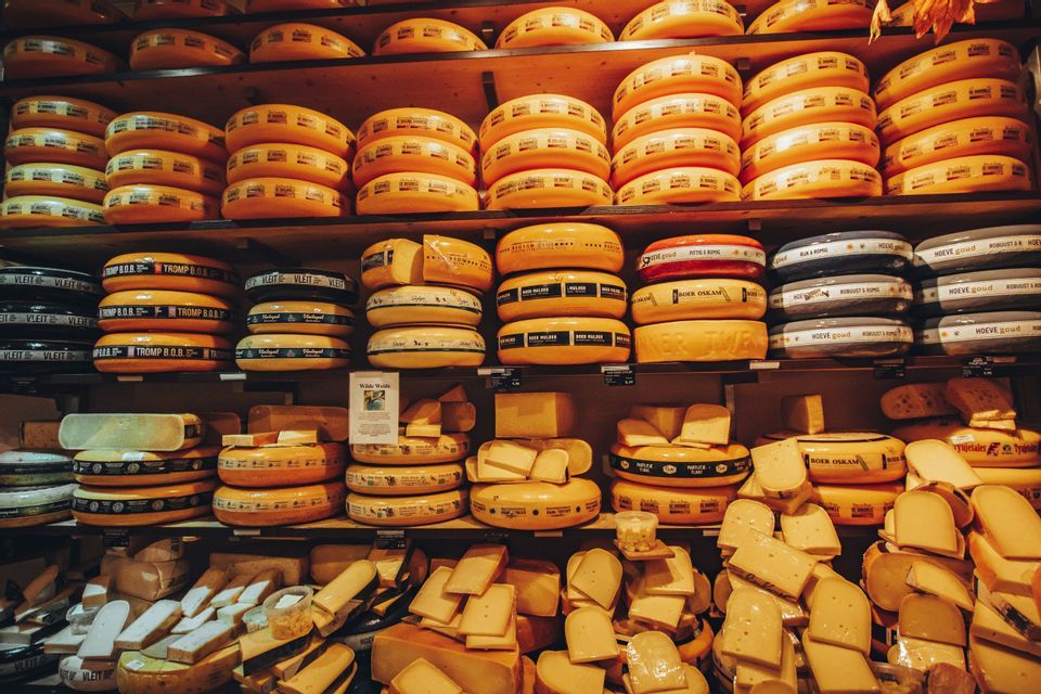 Una variedad de grandes ruedas de queso y rebanadas cortadas exhibidas en estantes de madera en una tienda.