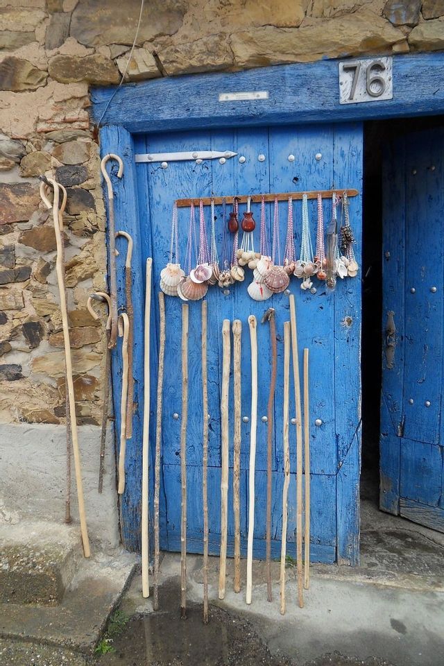 Bastones de madera y collares de conchas de vieira se exhiben sobre una puerta de madera azul brillante en una pared de piedra.