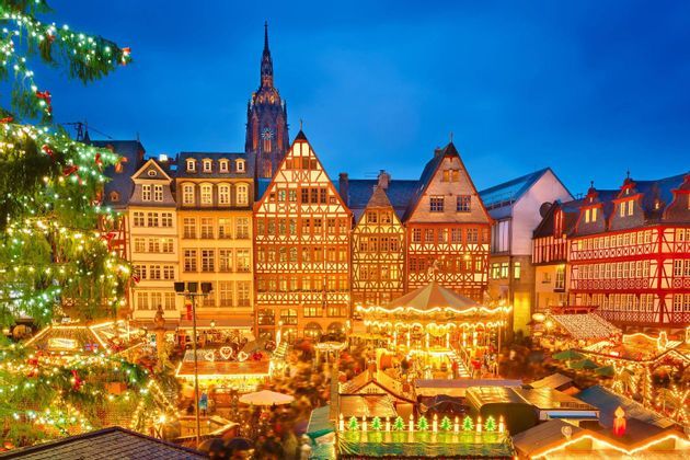 Un mercado navideño iluminado al anochecer, con un carrusel, puestos y edificios tradicionales de madera al fondo.