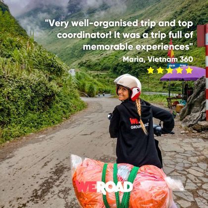 A woman from a WeRoad group trip smiles while riding a scooter on a winding road through lush green mountains.