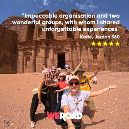 A WeRoad group trip smiles for a selfie in front of a large, ancient monument carved into a rock face.