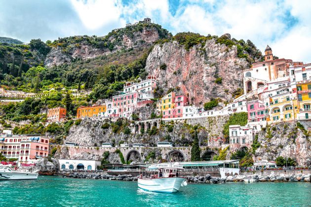 A WeRoad group trip on a tour boat sailing on turquoise water in front of a colorful village on a steep cliffside.