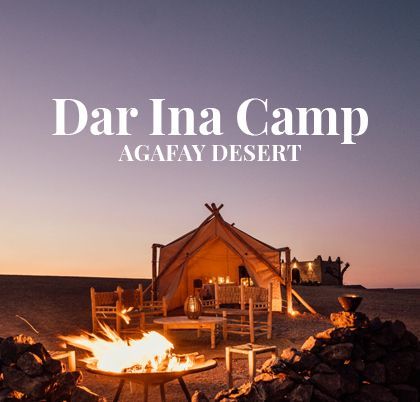Un falò arde in un braciere fuori da una tenda glamping illuminata nel deserto al crepuscolo.