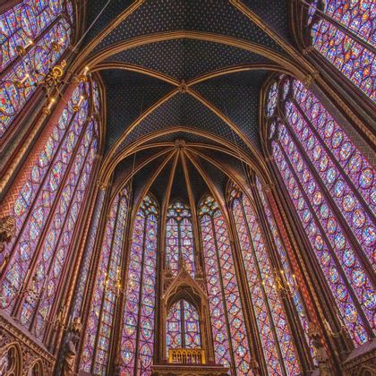 Una vista dal basso dell'interno di una cappella con imponenti e vivaci vetrate colorate e un soffitto a volta scuro decorato con stelle d'oro.