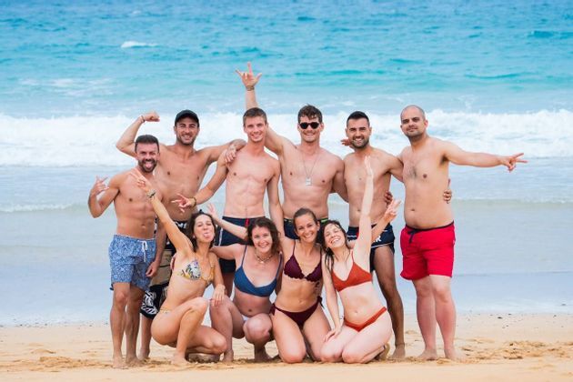 Un viaggio di gruppo WeRoad di uomini e donne in costume da bagno che posano e sorridono per una foto su una spiaggia sabbiosa.