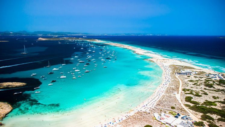 Vue aérienne d'un cordon de sable étroit avec des bateaux ancrés dans l'eau turquoise d'un côté et la mer d'un bleu profond de l'autre.