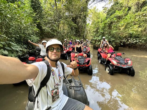 Un viaggio di gruppo WeRoad su quad rossi, in posa per un selfie, mentre attraversano un ruscello fangoso in una giungla fitta.