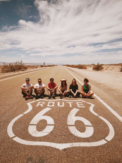 Un viaje en grupo de WeRoad posa en una carretera desierta, detrás del gran escudo de la Ruta 66 pintado en el asfalto.