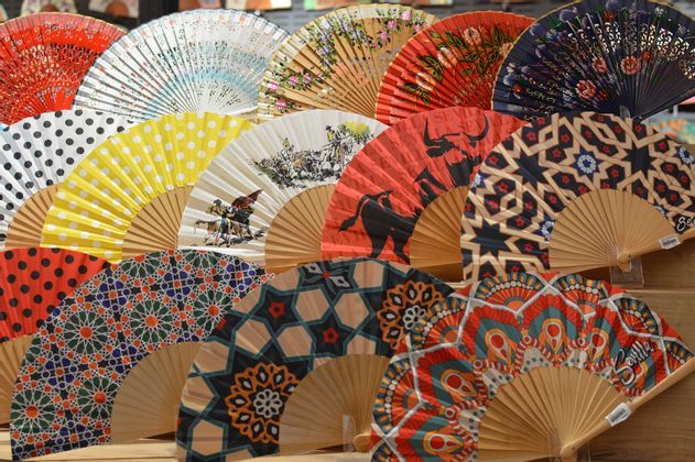 Una colección de coloridos abanicos españoles con varios patrones como lunares, formas geométricas y escenas taurinas.