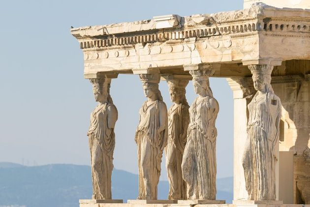 Cinque antiche cariatidi che sorreggono il tetto di un tempio classico sotto un cielo limpido e sereno
