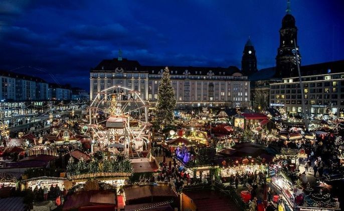 Un mercatino di Natale all'aperto illuminato di notte con una ruota panoramica, un albero decorato e bancarelle in una piazza della città.