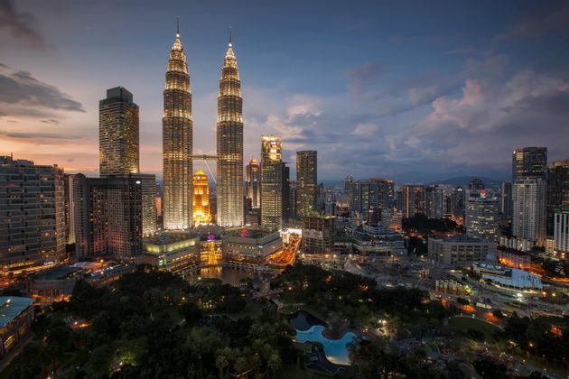 Le Torri Petronas illuminate e i grattacieli circostanti si ergono sopra un parco cittadino al tramonto.