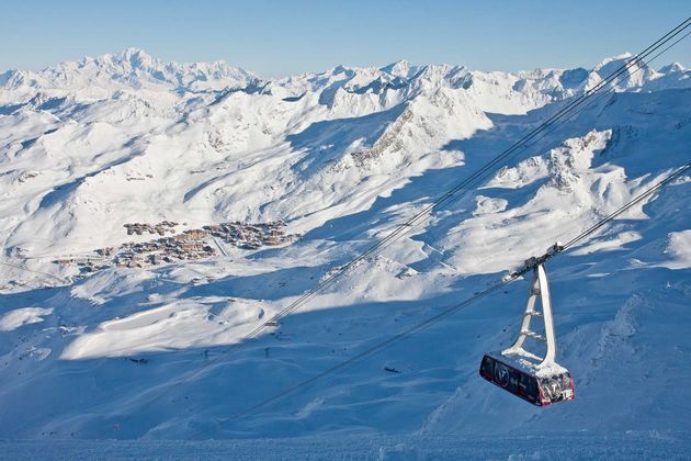 Una funivia viaggia in alto sopra una vasta valle montana innevata con una piccola località sciistica in lontananza.