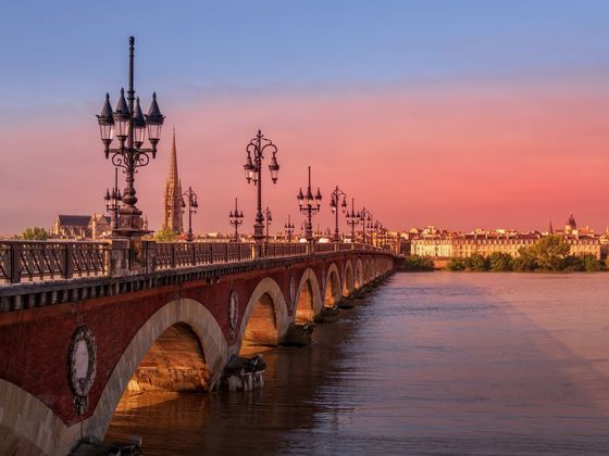 El Pont de Pierre de Burdeos sobre el Garona al atardecer, con las farolas encendidas y el horizonte de la ciudad al fondo.