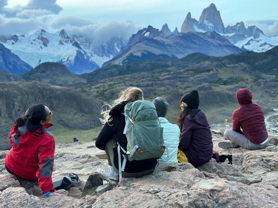 Un voyage de groupe WeRoad assis sur un point de vue rocheux, contemplant une chaîne de montagnes enneigées.
