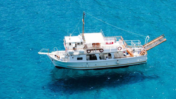 Veduta aerea di una barca bianca che galleggia in acqua limpida e turchese, con l'ombra visibile sotto.