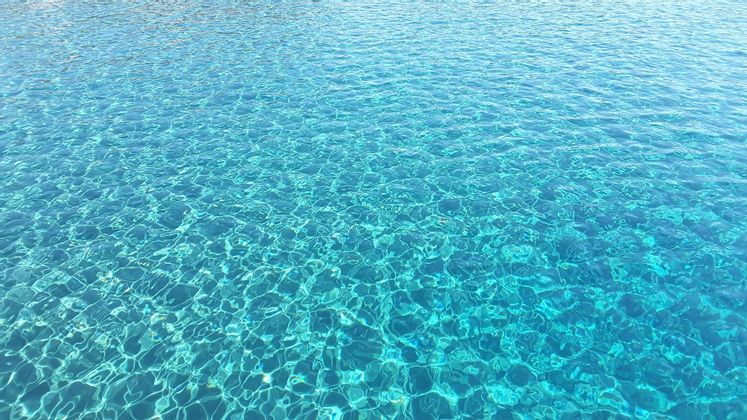 Il sole si riflette sull'acqua turchese limpida e increspata, creando un effetto scintillante.