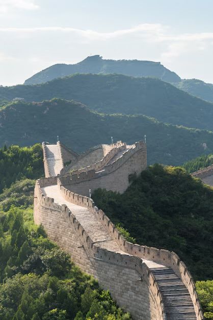 Una larga muralla de piedra con almenas serpentea por las cumbres de exuberantes montañas verdes bajo un cielo brillante.