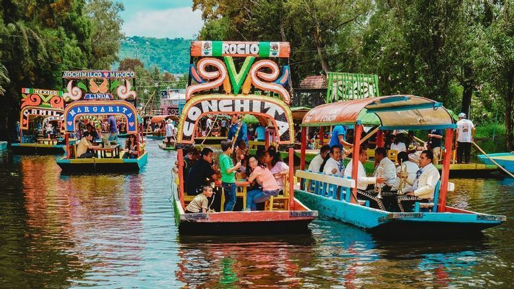 A WeRoad group trip travels by colorful boats on a busy waterway, alongside a boat carrying a mariachi band.