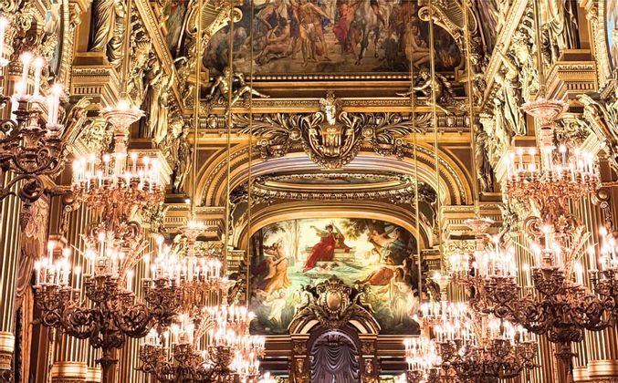 L'interno dorato e sfarzoso di un teatro dell'opera, con lampadari illuminati, intagli intricati e dipinti classici.