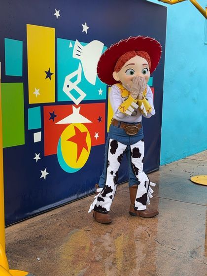 Jessie di Toy Story in costume posa con le mani alla bocca davanti a una parete grafica colorata.