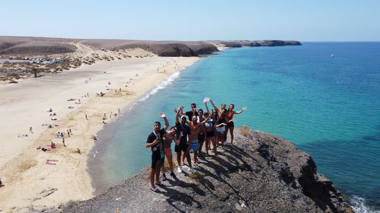 Un viaje en grupo de WeRoad posa para una foto en un acantilado rocoso con vistas a una playa de arena y un mar turquesa.