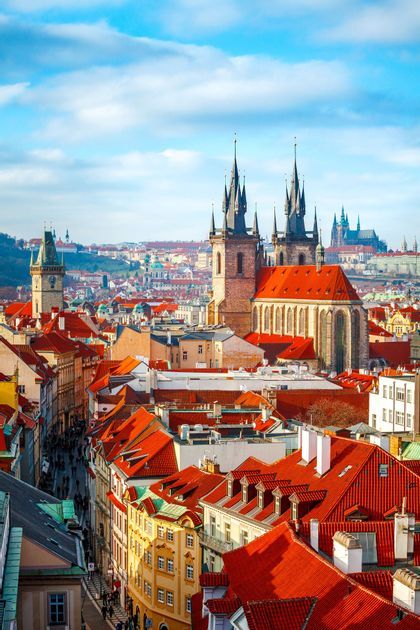 Eine Vogelperspektive auf eine historische europäische Stadt mit roten Ziegeldächern und einer prominenten gotischen Kirche mit zwei Türmen unter blauem Himmel.