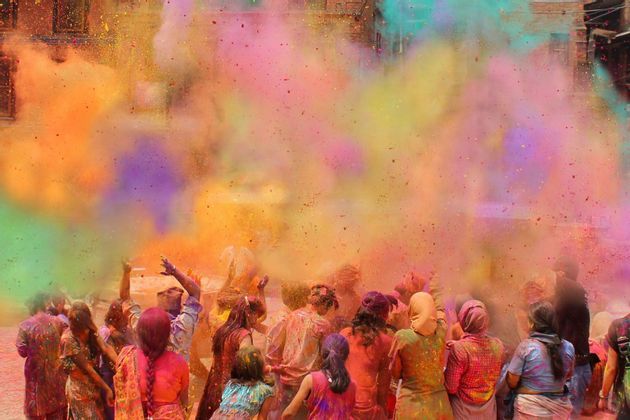 Un viaje en grupo de WeRoad de personas vistas de espaldas celebrando el festival Holi lanzando polvos de colores al aire.