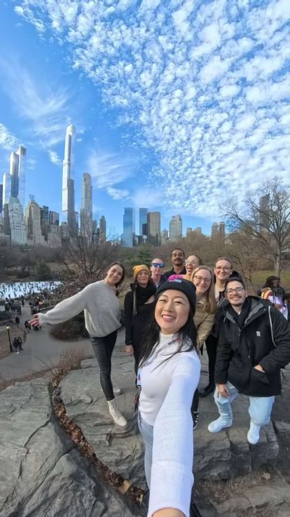 Eine Frau macht ein Selfie von ihrer WeRoad-Gruppenreise, posierend auf einem großen Felsen, mit einer Stadtsilhouette und einer Eisbahn im Hintergrund.