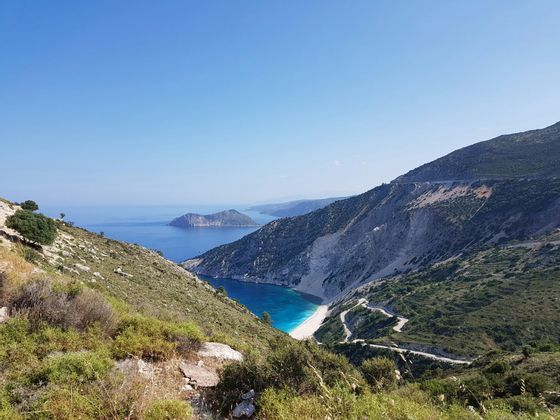 Una strada tortuosa si snoda lungo una scoscesa scogliera verdeggiante fino a una spiaggia di sabbia bianca appartata e un mare turchese.
