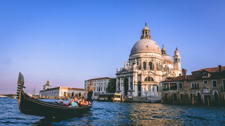 Un voyage de groupe WeRoad en gondole sur un canal, avec une grande basilique à dôme en arrière-plan sous un ciel dégagé.